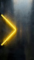 Yellow neon arrow glowing on a dark brushed metal surface, casting warm light, symbolizing direction, progress, and forward movement.