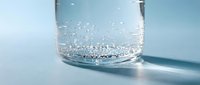 Clear glass with sparkling carbonated water bubbles rising to surface on clean white background for refreshing drink concepts and healthy lifestyle.