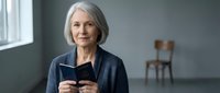 Confident senior Caucasian businesswoman with gray hair holding smartphone in modern office interior, professional mature female executive using mobile technology.