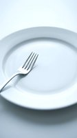 Empty white ceramic plate with a silver fork on a light background, symbolizing diet, fasting, or minimalist dining concept.