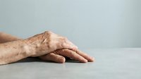 Elderly hands with visible veins and wrinkles resting on white surface against neutral background showing aging process and senior healthcare concepts.