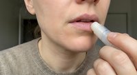 Woman applying lip balm stick to lips for skincare routine and moisturizing dry chapped lips in natural lighting close-up shot.