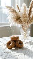 Fresh cinnamon sugar donuts stacked on marble table with pampas grass in crystal vase by window creating cozy bakery atmosphere for food photography.