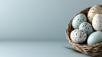 Speckled eggs in natural woven nest against soft blue background, featuring pastel blue and beige colored eggs with dark spots, creating minimal Easter composition.
