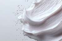 Smooth white cream texture with scattered dark particles against light background, cosmetic product swirl detail showing luxurious skincare consistency.