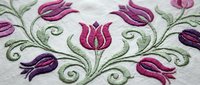 Elegant embroidered tulip pattern with pink and purple flowers on white fabric. Decorative floral design for textile crafts and home decor projects.