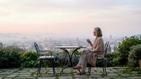Woman enjoying morning coffee on terrace overlooking city skyline at sunrise, peaceful lifestyle moment for relaxation and mindfulness content.