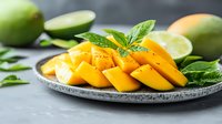 Fresh ripe mango slices arranged on gray ceramic plate with mint leaves and lime garnish against dark background, vibrant tropical fruit composition.
