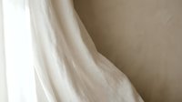 Soft flowing white fabric drapes elegantly against neutral beige wall creating minimalist textile background for interior design and fashion concepts.