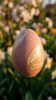 Speckled Easter egg with pastel pink and cream swirled pattern standing upright in green grass with soft bokeh spring garden background for holiday decorations.