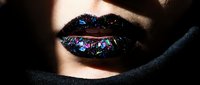 Close-up of lips with iridescent glitter makeup in blue and purple tones, partially covered by dark fabric. Suitable for beauty, cosmetics, and makeup artistry projects.
