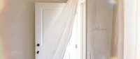 Soft light fills a bright entryway with sheer white curtain flowing in breeze, welcome sign on wall, airy minimal home interior.