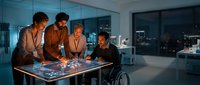 Diverse business team collaborating around interactive digital table in modern office at night analyzing data and planning strategy.