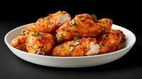 Spicy buffalo chicken wings garnished with fresh herbs served on white plate against dark background. Crispy, golden-brown coating with vibrant orange sauce.
