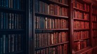 Vintage library interior with wooden bookshelves filled with old leather-bound books creating warm atmospheric lighting for academic research spaces.