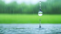 Water drop falling and creating splash on water surface against blurred green nature background, capturing moment of impact with rain in background.