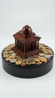 Wooden miniature government building surrounded by coins on circular base representing financial policy and economic investment concepts.