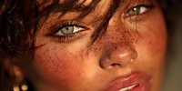 Young woman with freckles and striking green eyes in warm sunlight. Natural beauty portrait with golden hour lighting for skincare and cosmetics campaigns.