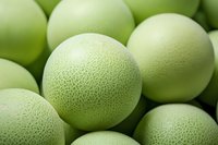 Fresh honeydew melons with textured pale green rind in macro view, showing natural pattern detail perfect for food photography, healthy eating concept and menu design.