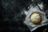 Fresh baked bread roll dusted with flour on white parchment paper against dark moody background with copy space for bakery menu or food photography.