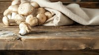 Fresh white mushrooms scattered on rustic wooden table with natural linen cloth, moody lighting creates warm atmosphere for food photography and cooking.