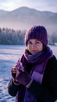 Young woman in purple knit hat and scarf enjoying hot drink outdoors in snowy mountain landscape during winter sunset with warm golden light and peaceful atmosphere.