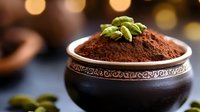 Rich cocoa powder in ornate ceramic bowl topped with green pistachios against warm bokeh background for culinary and baking projects.