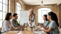 Diverse team of young professionals collaborating in modern loft office with exposed brick, laptops, and whiteboard during creative brainstorming meeting.