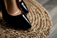Elegant black patent leather high heel shoe on natural jute round rug against wooden floor background, showcasing luxury fashion and home decor elements.
