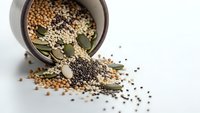 Mixed spices and seeds spilling from ceramic bowl on white background. Coriander, peppercorns, bay leaves scattered for cooking and seasoning recipes.