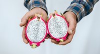 Hands holding halved dragon fruit with white flesh and black seeds against white background, showcasing fresh tropical produce for culinary and wellness content.