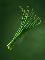 Fresh green asparagus spears arranged in bundle against dark green background, dramatic lighting highlights natural texture and form. Suitable for culinary content.