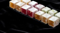 Colorful Turkish delight lokum candy cubes with powdered sugar arranged on dark plate. Traditional Middle Eastern confectionery sweets for dessert menu.