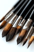 Close-up of professional art brushes with natural bristles and metal ferrules on black handles, arranged in row on white surface.