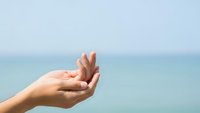 Open cupped hands reaching upward against serene ocean backdrop, symbolizing hope, prayer, and receiving blessings by the peaceful seaside.