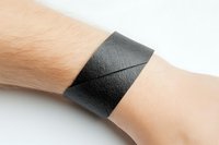 Close-up of black leather cuff bracelet worn on wrist against white background. Unisex accessory for fashion, jewelry design, and lifestyle applications.