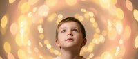 Young boy looking up with wonder against golden bokeh lights background creating magical dreamy atmosphere for holiday celebrations and childhood dreams.