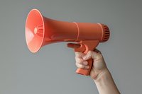 Hand holding red megaphone against neutral gray background, demonstrating announcement and communication concept for marketing and public speaking purposes.