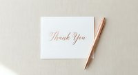 Elegant thank you card with rose gold calligraphy and matching pen on neutral background for wedding stationery and special occasions.