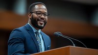 Confident African American male executive in navy suit and glasses delivering speech at podium, expressing positive leadership during business presentation.