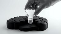 Hand in black glove placing glowing light bulb into brain-shaped puzzle piece holder representing innovation and creative problem solving concepts.