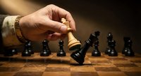 Hand moving white king chess piece on wooden board with black pieces in strategic business game representing leadership and decision making.