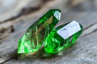 Vibrant emerald green crystal formations on weathered wood surface showcase natural mineral structure with translucent facets and light reflections in macro photography.