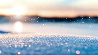 Sparkling snow surface with bokeh effect and soft sunset light creating magical winter atmosphere. Blurred natural background with falling snowflakes and glitter.