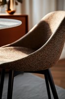 Modern upholstered dining chair with curved seat in brown textured fabric and black metal legs, close-up view showing elegant minimalist design in soft lighting.