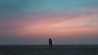 Romantic couple silhouette embracing on beach at sunset with pink and blue sky colors creating peaceful evening atmosphere for love and relationship concepts.