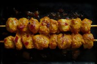 Grilled chicken skewers with golden marinade and charred edges on dark background, juicy meat pieces threaded on wooden sticks showing traditional BBQ cooking.