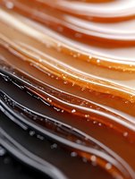Swirling caramel sauce with tiny bubbles creating abstract waves and lines in warm amber and dark brown tones, macro photography showing rich texture and flow.