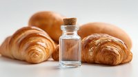 Fresh baked croissants with small glass bottle of extract or essence on white background, food photography for bakery or culinary concept.