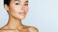 Young Asian woman with natural makeup, glowing healthy skin, and bare shoulders against light background, expressing confidence and beauty in minimalist portrait.